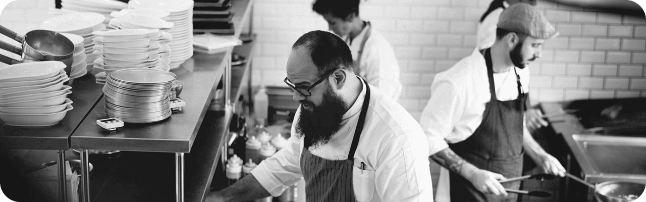 Three chefs working diligently in a professional kitchen, preparing various dishes.